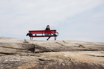 A huge stone, on which among the trees stands a lonely bench, a bench against the blue sky