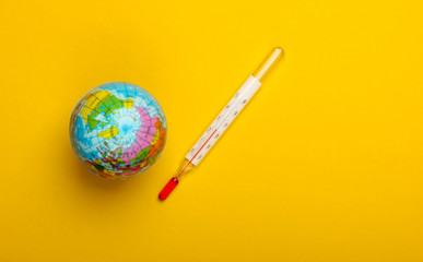Global warming still life. Globe and thermometer on a yellow background. Global climate issues. Eco...