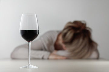 Glass with alcohol on blurred view of a lonely and desperate drunk woman