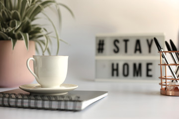 Home office desc with cup of coffee, stationary, home plant and Stay Home sign. Stay  home concept,  office desc concept during pandemic