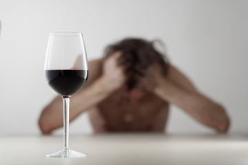 Glass with wine/ alcohol on blurred view of a lonely and desperate drunk man