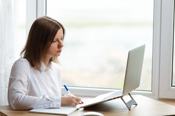 Young woman sitting at working table with laptop and notepad.