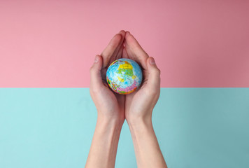Globe in a female palms on blue pink pastel  background. Planet earth care concept