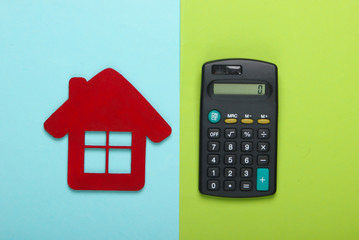 Calculation of the cost of rental housing. Red house figurine, calculator on a blue-green background. Top view