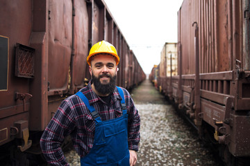 People working for shipping companies transporting goods all over the world. Portrait of smiling railroad worker standing between freight trains.