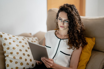 chica joven con gafas trabajando desde el sofá de su casa con una tablet