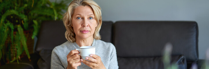 Delicious drink.Elderly woman sitting on the sofa in her living room and holding a cup of coffee