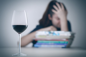 Glass with alcohol on blurred view of a lonely and desperate drunk woman lying on a stack of books .
