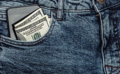 Hundred dollar bills and a smartphone in the front pocket of blue jeans close-up.