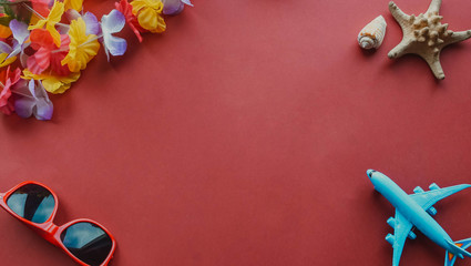 Top view essential travel items. airplane, sunglasses, starfish, hawaiian necklace on red background.Free space for creative design text and word. Flat lay different object for mock up.