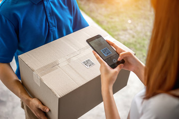 A young Asian deliveryman is delivering a package of women in front of her house. And asked her to scan the QR code after she made an online order during the coronavirus or Covid-19 virus outbreak.