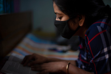 Portrait of an Indian young woman wearing corona preventive mask in home isolation in front of a window. Indian lifestyle and disease.