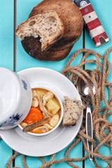 Fresh fish soup in plate on sea background, top view