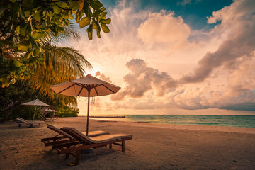 Beautiful tropical sunset scenery, two sun beds, loungers, umbrella under palm tree. White sand, sea view with horizon, colorful twilight sky, calmness and relaxation. Inspirational beach resort hotel