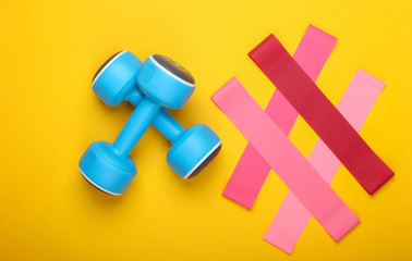 Dumbbells with fitness elastic bands on a yellow background. Top view, flat lay