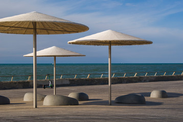 Empty embankment in Tel Aviv, Israel. View of umbrellas and stone benches to relax in a sunny day. The sea and the scooter in the background.
