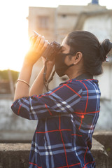 Back light portrait of an Indian young woman with corona preventive mask taking photographs on a rooftop in home isolation.Indian lifestyle, disease and home quarantine.