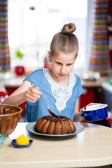 Young kid is making, easy to prepare and healthy, home made Easter cake - during stay at home. She is decorating the cake with dark chocolate.