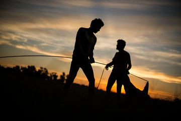 Fototapeta na wymiar Silhouettes of two men setting a tent at sunset