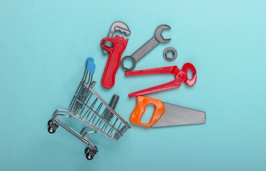 Mini shopping trolley with a toy tool on a blue pastel background. Top view