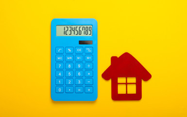 Calculation of the cost of rental housing. Red house figurine, calculator on yellow background. Top view
