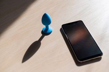 Blue anal plug synchronizing with a smartphone. Latex vibrator delivering for carnal pleasures.