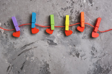 rainbow colored wooden clothespins with clamped red hearts on grey concrete background. Pride day concept, flat lay