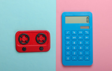 Calculation of gas or electricity costs. Calculator and toy kitchen stove on blue-pink pastel...