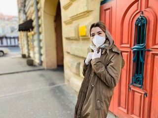 young woman in a coat. Stylish young woman in protective mask and white gloves against coronavirus, walking on the old street. Covid-19.