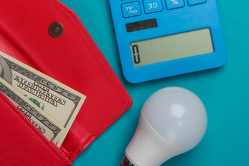 Energy and money saving. Calculators with led light bulb and wallet with dollar bills on blue background. Top view