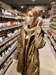 Fototapeta premium young woman shopping in supermarket. beautiful girl in a protective flu mask, goggles and gloves in a store, holds goods, purchases during quarantine - against coronavirus