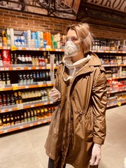 Fototapeta premium woman shopping in supermarket. beautiful girl in a protective flu mask, goggles and gloves in a store, holds goods, purchases during quarantine - against coronavirus