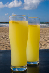Beach vacation: two glasses of lemonade stand on a table on the beach. Sand and sea in the background.