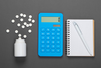 Calculation of the cost of medical expenses. Calculator, notebook and pills bottle on gray background. Top view. Minimalism