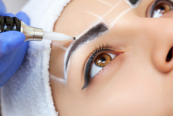 Permanent make-up for eyebrows of beautiful woman with thick brows in beauty salon. Closeup...