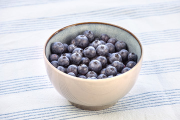 Bowl full with blueberry fruits on the kitchen table with tablecloth. Bilberries in bowl, healthy breakfast. 