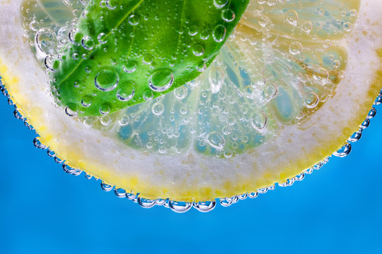 Lemon slice and Basil leaf and water bubbles on a blue background close-up.