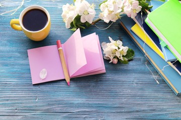 
Cup of coffee, blank notebook for notes, a stack of books, apple flowers on a wooden windowsill, home comfort concept