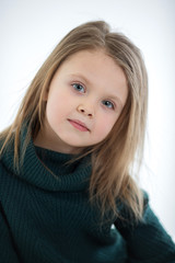 Cute blonde girl with straight hair with a light cute smile on a white background. Close-up portrait of a child. Look at the camera.