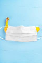 Yellow ripe banana covered with a white medical protective mask on a wooden light blue background