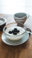 breakfast on a table, set with a cup of coffee and a natural yogurt with blackberries