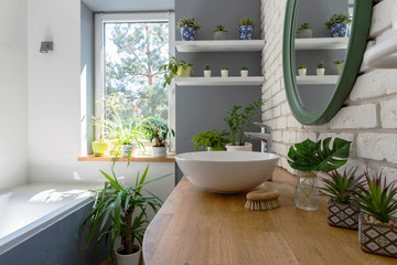 White bathroom with window and green plants. Cozy interior with wooden counter, brick wall, ceramic...