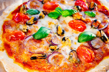 Seafood Italian homemade pizza with mussels, fresh herbs, basil, tomatoes,  red onion and mozzarella on a wooden board. Natural sunny light, close up view.