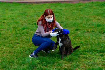 Young female using a face mask as a coronavirus spreading prevention walking with her dog. Global COVID-19 pandemic concept image.