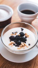 breakfast on a table, set with a cup of coffee and a natural yogurt with blackberries, chocolate chips and pine nuts on top