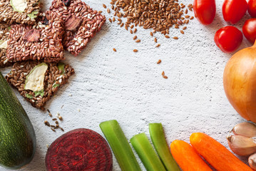 Healthy snack: crispbread with cereal multigrain flax seed, sesame, flaxseed, tomatoes, zucchini, carrots, celery stalks, beetroot, garlic around white background with copy space. Raw dry vegan food