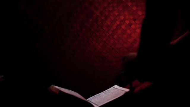 The Quran, the Muslim holy book, with misbaha or the Islamic prayer beads on the rihal or a wooden book stand in a rural room lit by a traditional oil lamp. Ramadan-themed video background.
