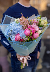 Strong man holding a delicate bouquet of beautiful flowers in his hands. Delicate flower bouquet. Wrapped flowers bouquet. Fresh beautiful flower. Man holding a big beautiful flowers bouquet.