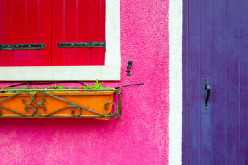 Violet wooden door, window with red shutters and pink wall. Close up view. Colorful architecture in Burano island, Venice, Italy.