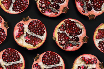 Pattern of ripe pomegranates on a black background. Slices of pomegranate with grains. A top view of a flat layout.